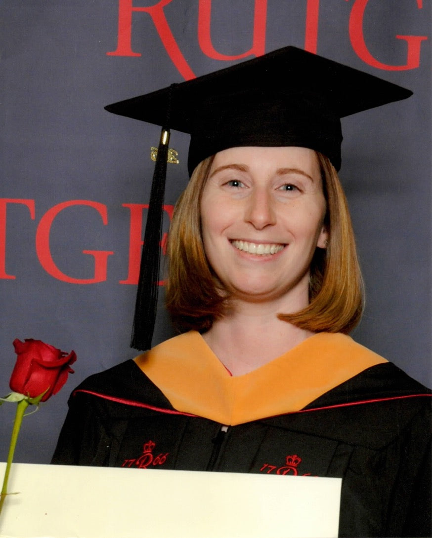 Graduate in cap and gown holding a red rose against a Rutgers backdrop